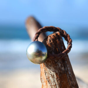 Bague en cuir marron tressé avec une perle de Tahiti de 12,5 mm, posée sur du bois flotté