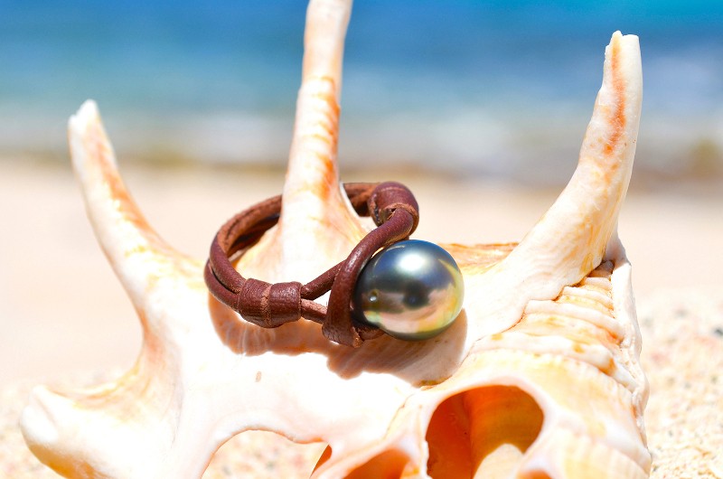 Leather ring with a 10 mm Tahitian pearl displayed on a shell by the sea