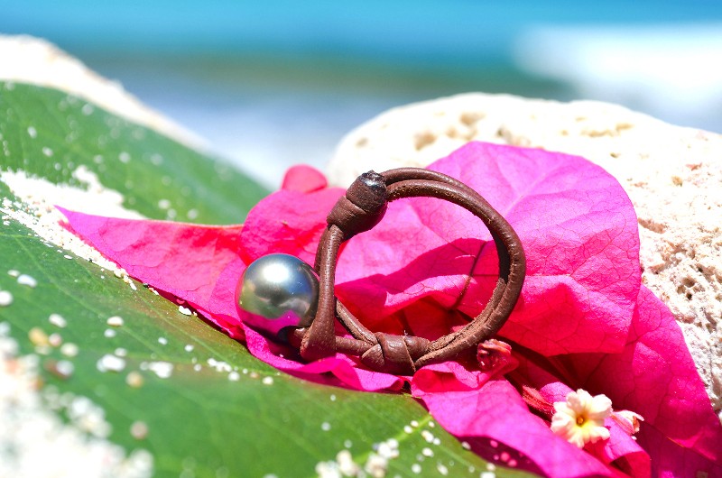 Leather ring with a 10 mm Tahitian pearl displayed on a pink flower by the sea