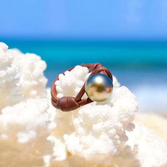 Brown leather ring with a 10 mm Tahitian cultured pearl displayed on coral by the sea