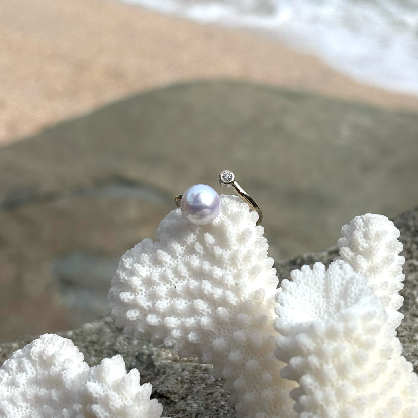 Adjustable white gold ring with a diamond and a white cultured pearl displayed on coral by the sea