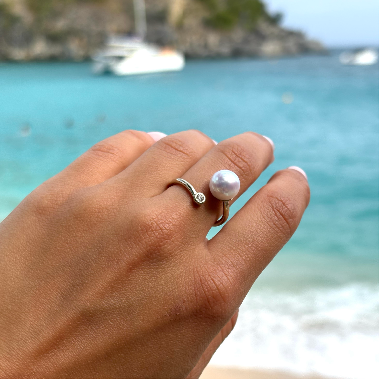 Adjustable white gold ring with a diamond and a white pearl worn on the hand by the sea