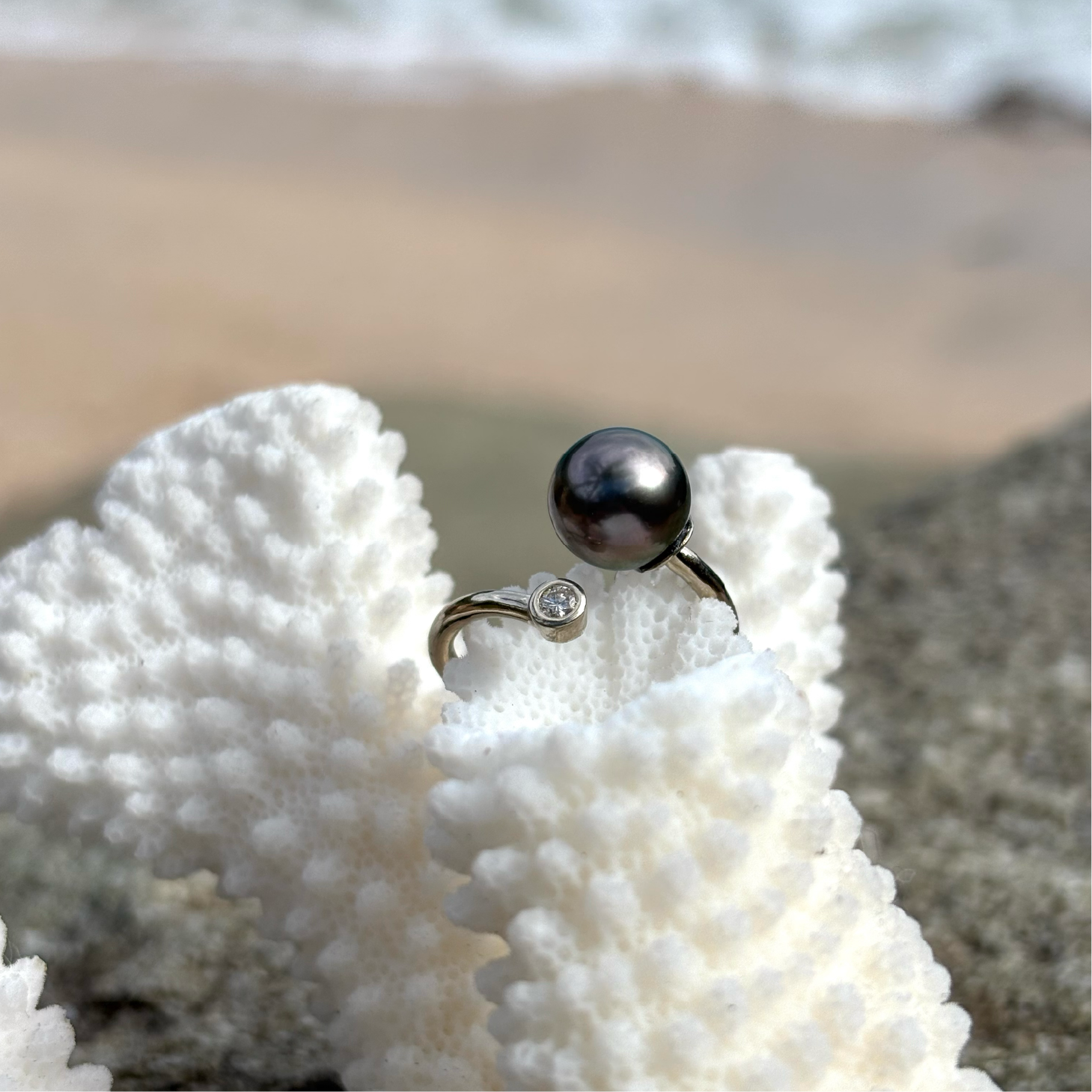 Adjustable white gold ring with a diamond and a black pearl displayed on coral by the sea