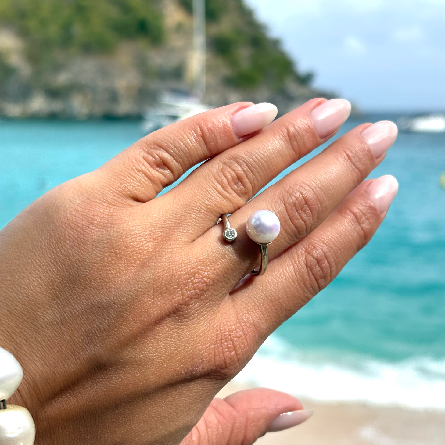 Adjustable yellow gold ring with a diamond and a white cultured pearl worn on the hand by the sea
