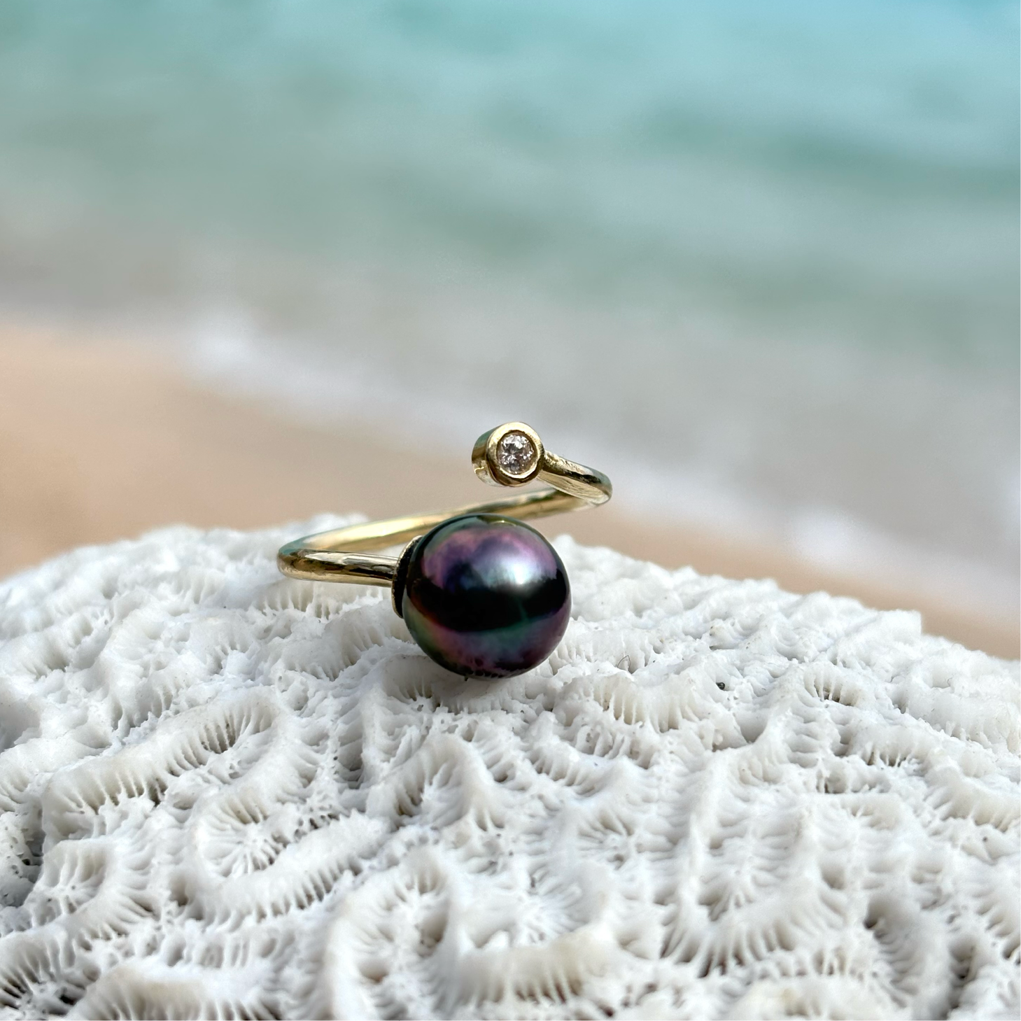 Adjustable yellow gold ring with a diamond and a Tahitian pearl displayed on coral by the sea