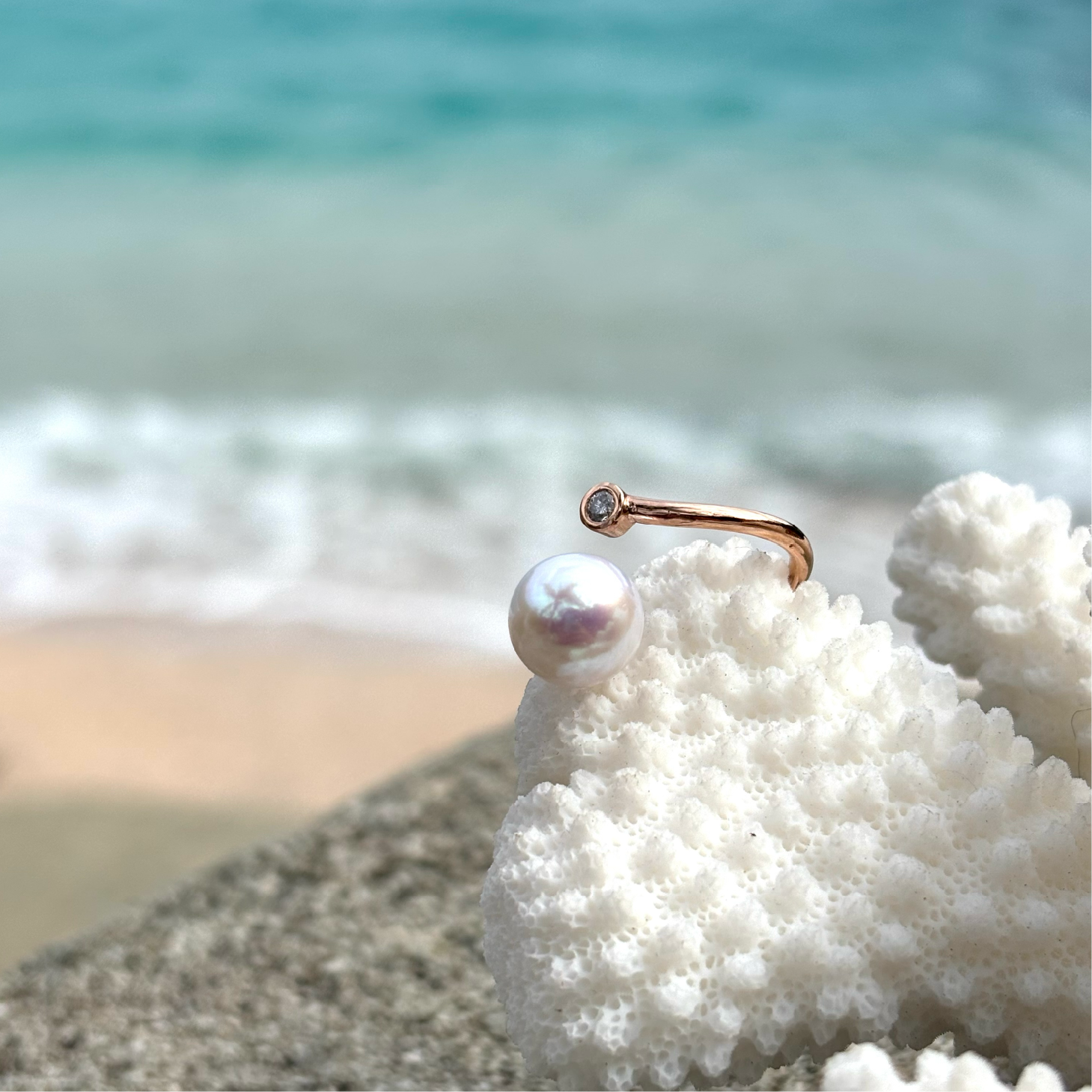 Adjustable rose gold ring with a diamond and a white pearl displayed on coral by the sea