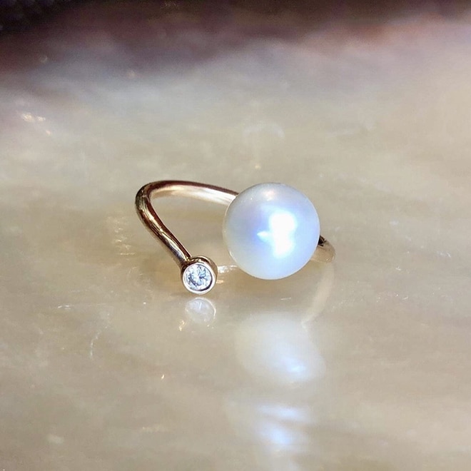 Adjustable rose gold ring with a diamond and a white cultured pearl displayed on mother-of-pearl