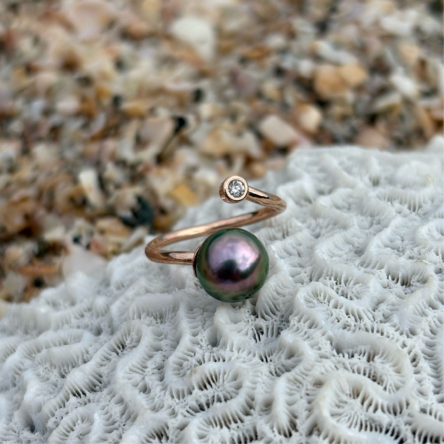 Adjustable rose gold ring with a diamond and a Tahitian pearl displayed on white coral by the sea
