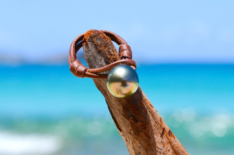 Leather ring with a 10.5 mm Tahitian pearl displayed on driftwood by the sea