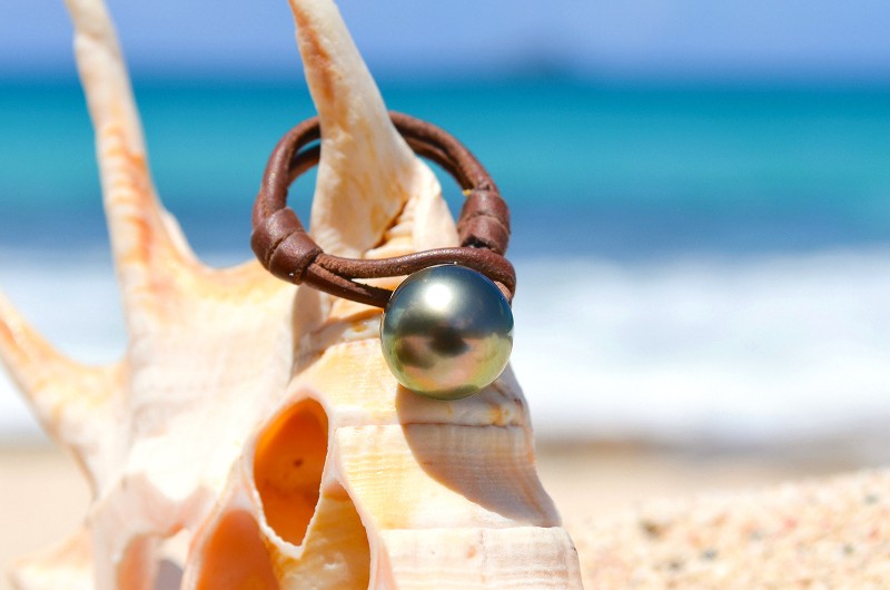 Leather ring with a 10.5 mm Tahitian pearl displayed on a shell by the sea