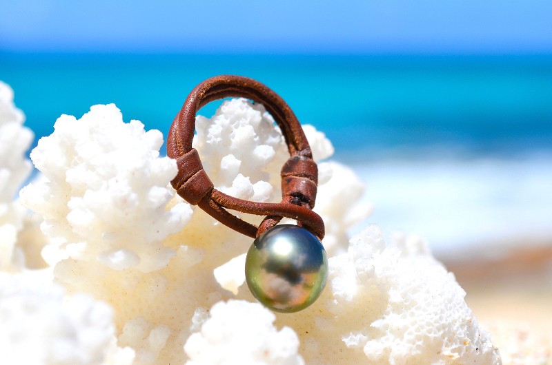 Leather ring with a 10.5 mm Tahitian pearl displayed on white coral by the sea