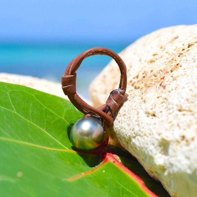 Brown leather ring with a 10.5 mm Tahitian cultured pearl displayed on a leaf by the sea