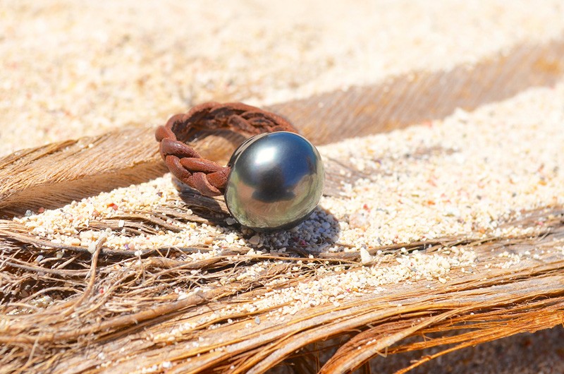 Bague en cuir tressé avec une perle de Tahiti de 15 mm présentée sur du bois et du sable