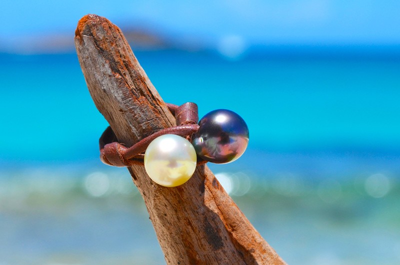 Bague Toi et Moi en cuir avec une perle de Tahiti et une perle blanche d’Australie de 11 mm présentée sur du bois flotté face à la mer
