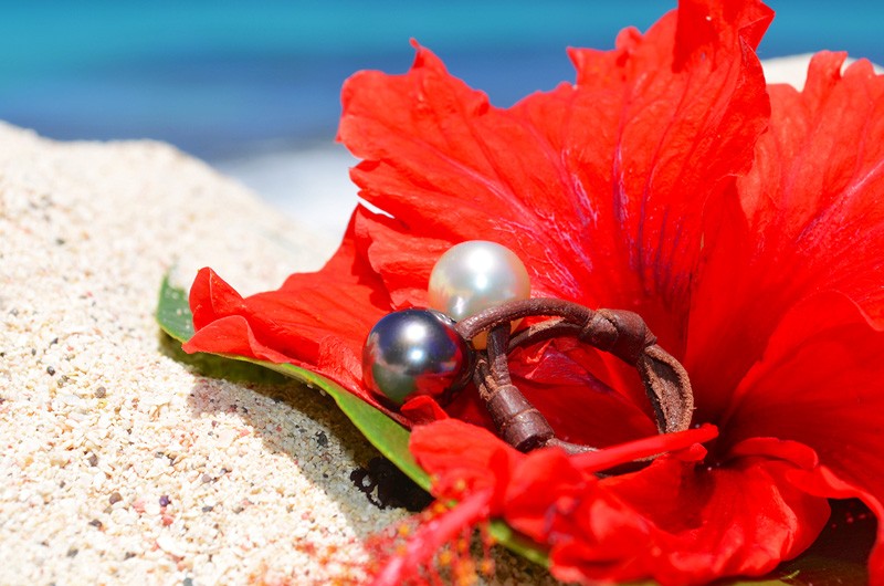 Bague Toi et Moi en cuir avec une perle de Tahiti et une perle blanche d’Australie de 11 mm présentée sur une fleur rouge face à la mer