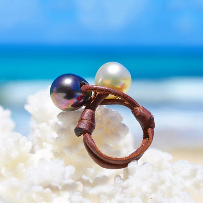 Bague Toi et Moi en cuir marron avec une perle de Tahiti et une perle blanche d’Australie de 11 mm présentée sur du corail blanc face à la mer