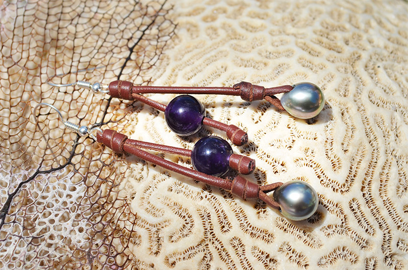 Leather earrings with amethysts and Tahitian pearls displayed on coral with a sea fan