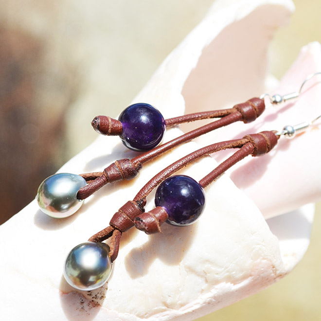 Brown leather drop earrings with amethysts and Tahitian pearls displayed on a seashell