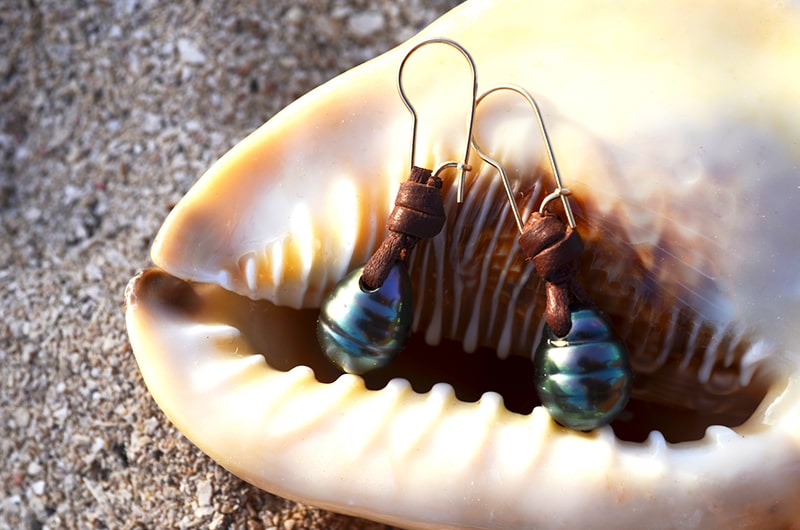 Leather earrings with drop-shaped Tahitian pearls displayed inside a seashell