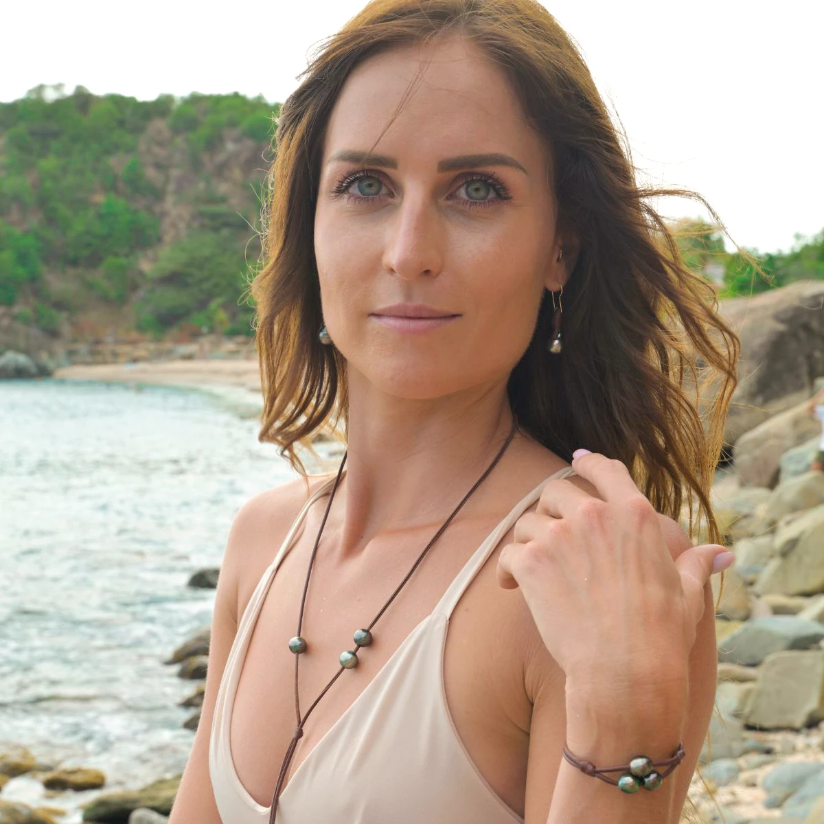 Leather earrings with drop-shaped Tahitian pearls worn by the sea