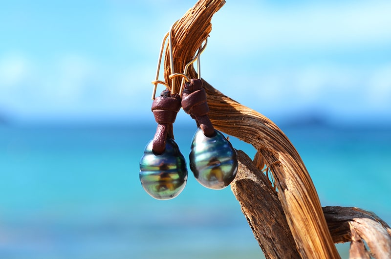 Leather earrings with drop-shaped Tahitian pearls suspended from wood by the sea