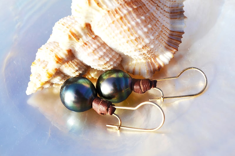 Leather earrings with semi-round Tahitian pearls displayed with a seashell