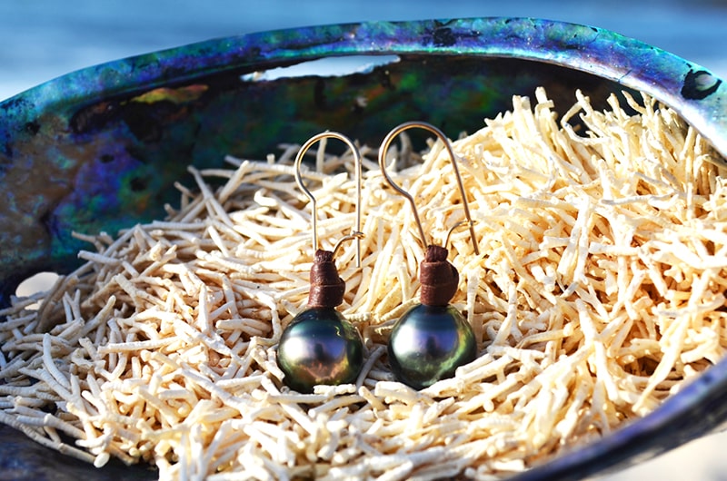 Leather earrings with semi-round Tahitian pearls displayed on natural fibers