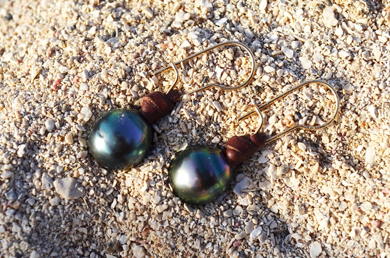 Leather earrings with semi-round Tahitian pearls displayed on sand
