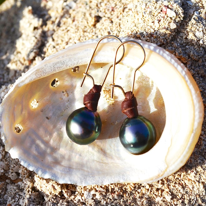 Brown leather earrings with two semi-round Tahitian pearls displayed inside a seashell