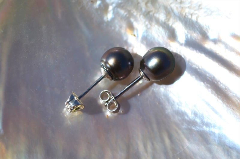 View of the settings and butterfly backs of sterling silver stud earrings with 8 mm Tahitian pearls on mother-of-pearl