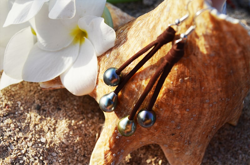 Leather drop earrings with four Tahitian pearls displayed on wood with white flowers