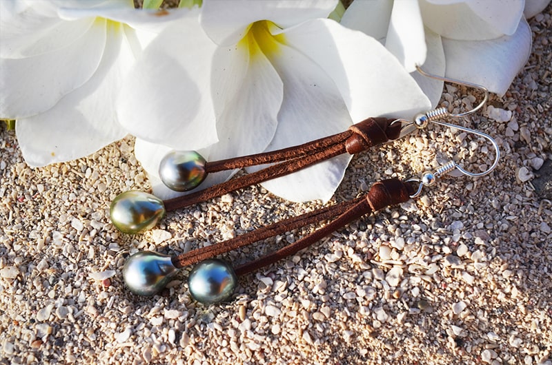 Leather drop earrings with four Tahitian pearls displayed on coral with white flowers