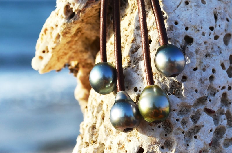 Leather drop earrings with four Tahitian pearls displayed on coral by the sea
