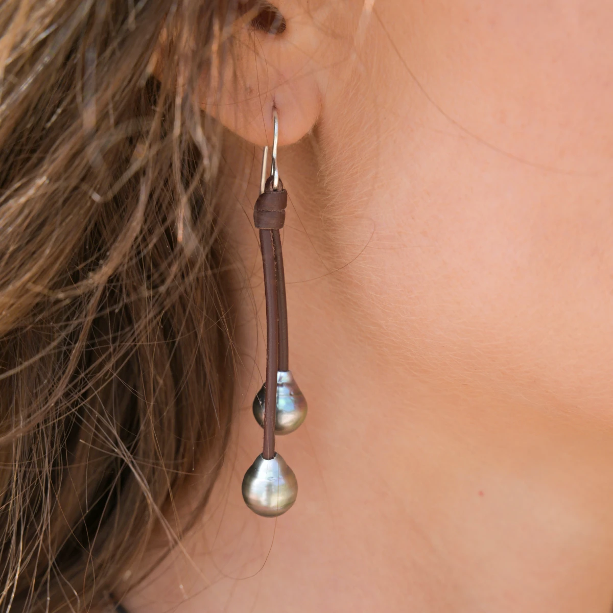 Close-up of leather drop earrings with four Tahitian pearls being worn