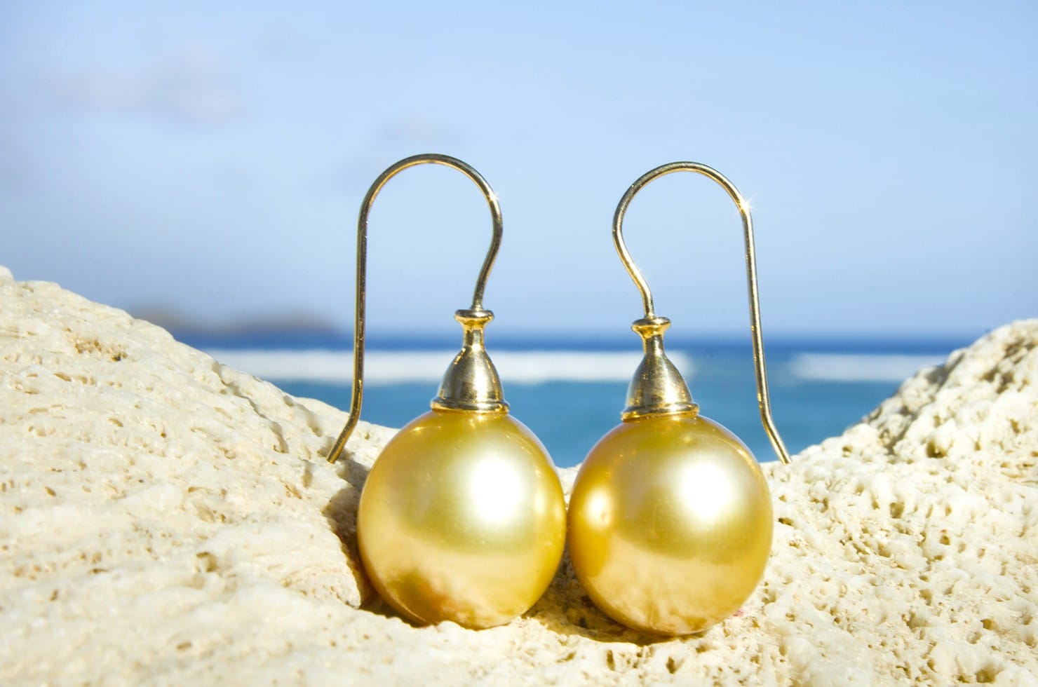 Boucles d’oreilles avec perles dorées d’Australie de 12 mm présentées sur du corail face à la mer