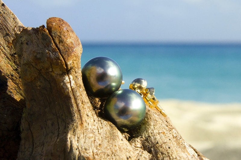 Earrings with 9.5 mm Tahitian pearls displayed on wood by the sea