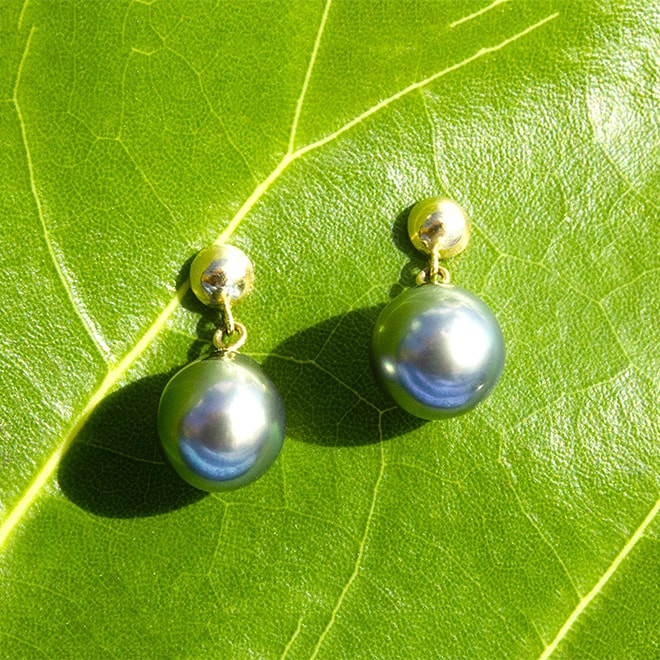Earrings with 9.5 mm Tahitian pearls displayed on a green leaf