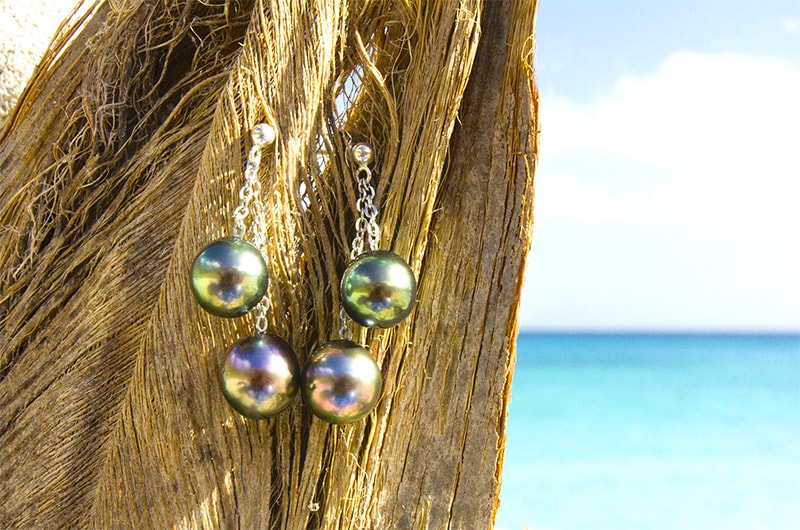 Sterling silver earrings with four Tahitian pearls displayed on wood by the sea