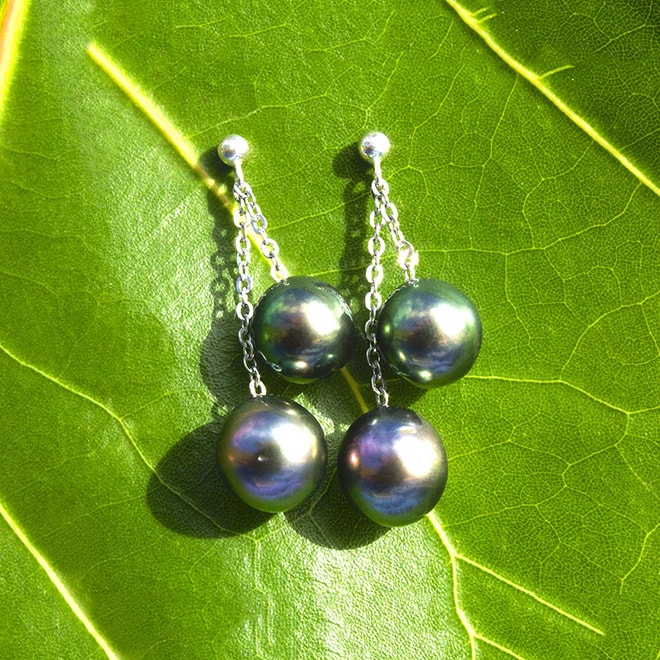 Sterling silver drop earrings with four Tahitian pearls displayed on a green leaf