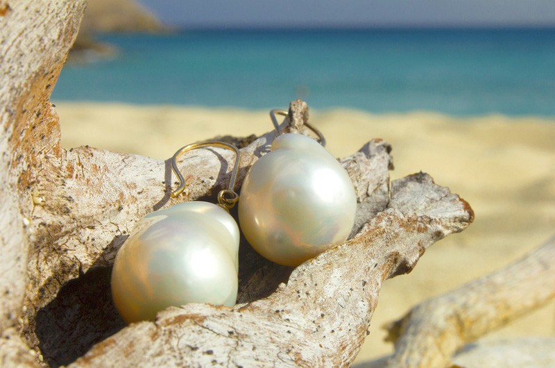 Gold earrings with white freshwater pearls displayed inside a seashell by the sea