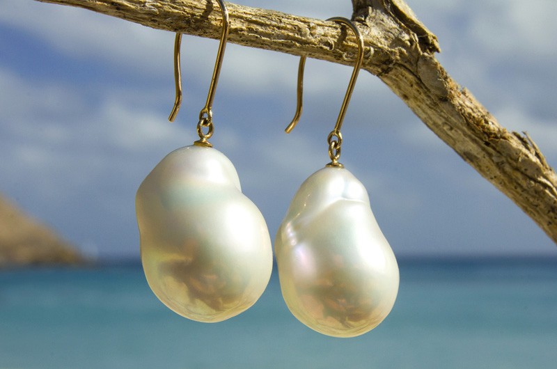Gold earrings with white freshwater pearls suspended from wood by the sea