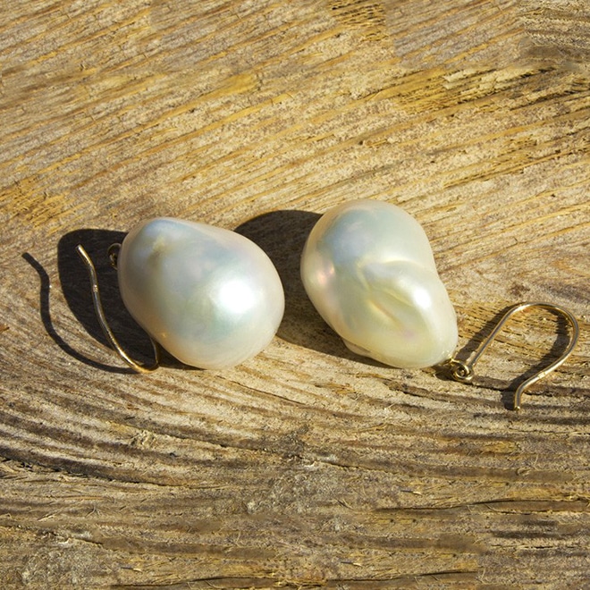 Gold earrings with white freshwater pearls displayed on wood