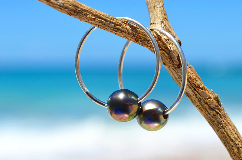 Créoles avec perles rondes de Tahiti suspendues à du bois face à la mer