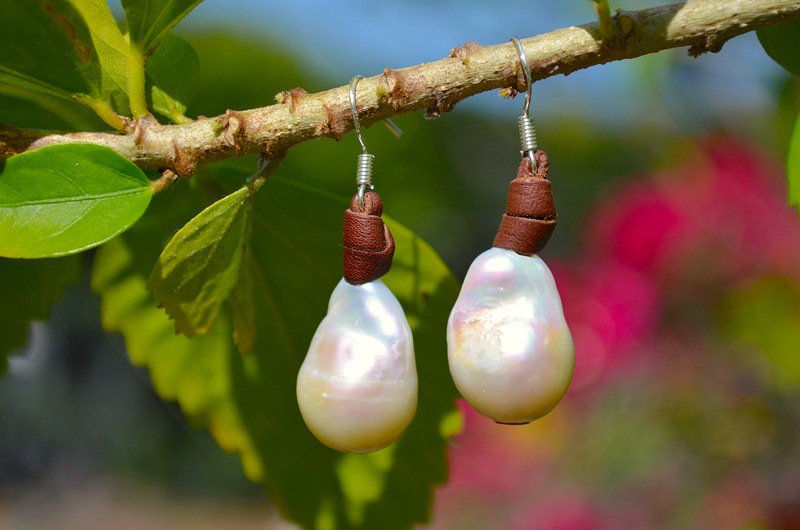 Leather earrings with white freshwater pearls suspended from a branch in a garden