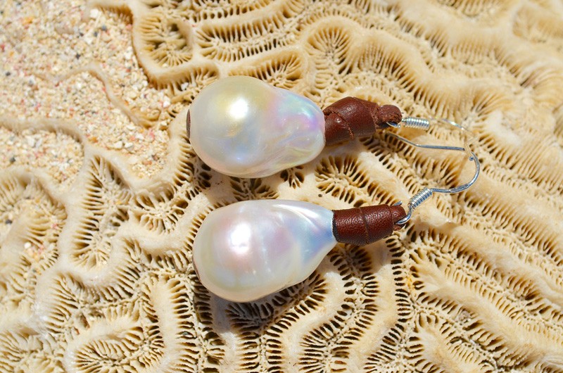 Leather earrings with white freshwater pearls displayed on white coral