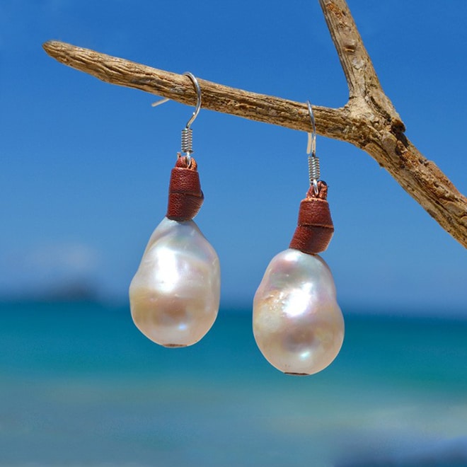 Brown leather earrings with white freshwater pearls suspended from wood by the sea
