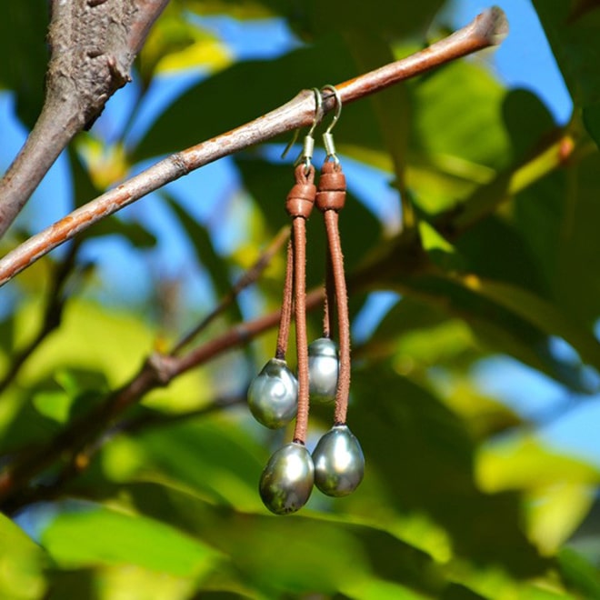 Brown leather earrings with four Tahitian pearls suspended from a branch in a garden