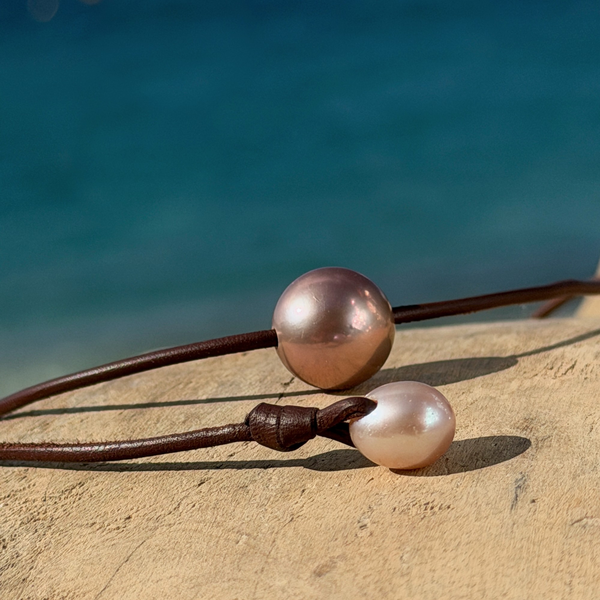 Ras du cou en cuir et grande perle rose de 14 mm, sur du bois, détail.