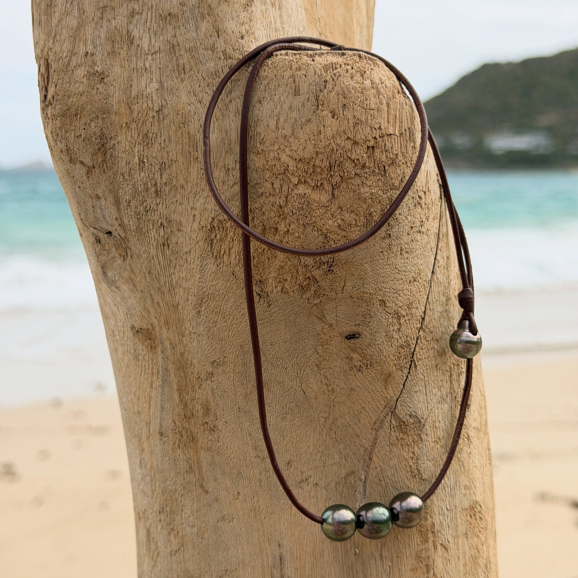 Ras du cou en cuir et trio de perles de Tahiti de 11,5 mm, sur du bois.
