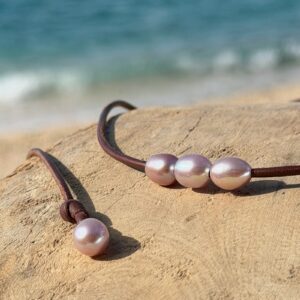 Ras du cou en cuir et trois perles roses ovales, sur du bois, détail.